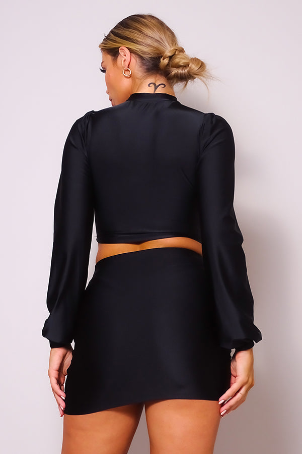 Ensemble blouse à col roulé et découpe sur le devant, manches longues bouffantes, et mini-jupe à volants froncée sur les côtés.